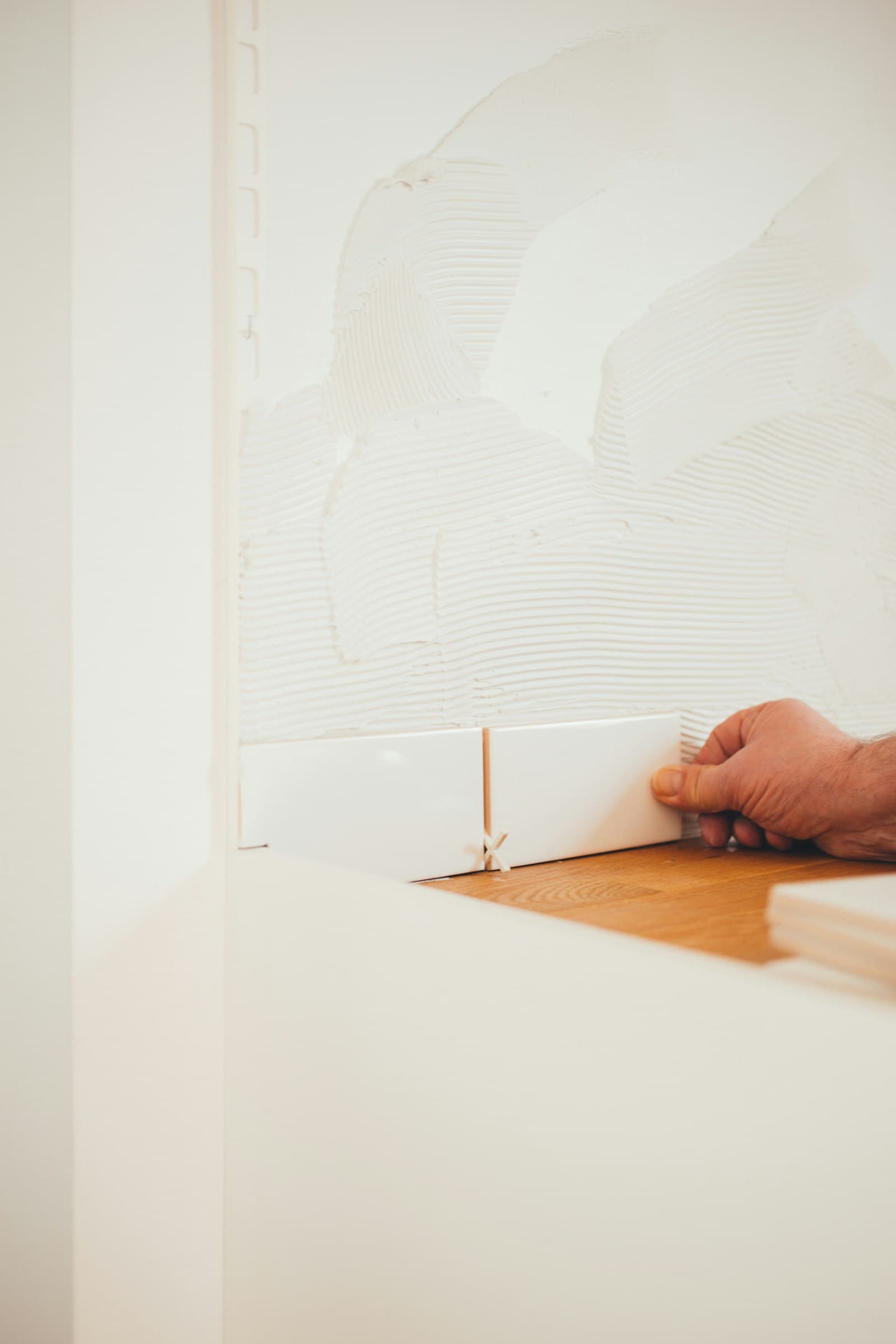 Hand setting subway tile on a fresh thinset-combed wall mid-installation