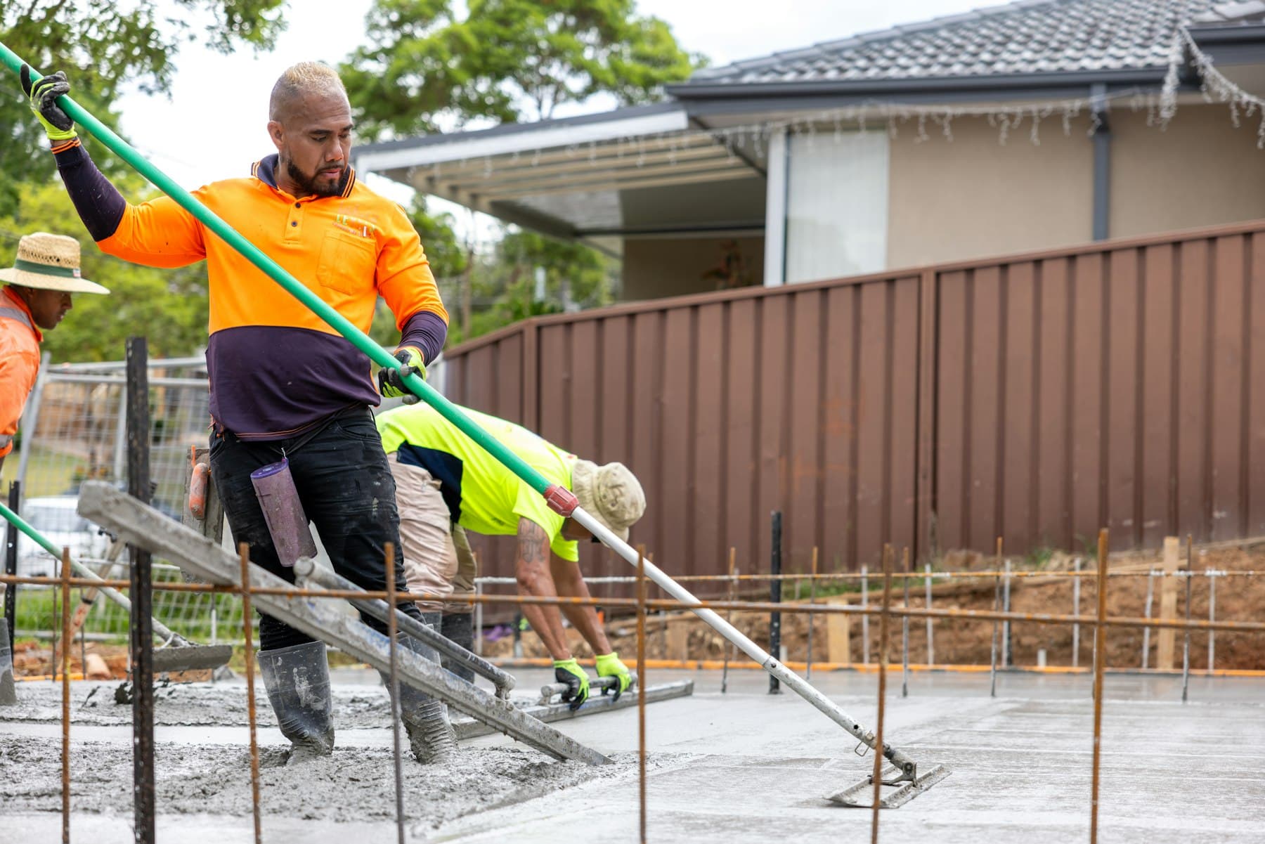 Crew screeding and finishing a freshly poured residential concrete slab with rebar formwork